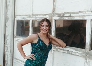Woman in emerald green sequin gown leaning against weathered white barn doors smiling. Senior grad photos. Graduation photos.