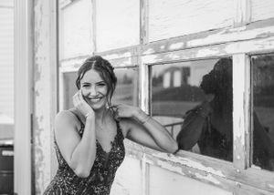 Black and white portrait of smiling woman in sequin dress leaning against rustic window. Senior grad photos. Graduation photos.