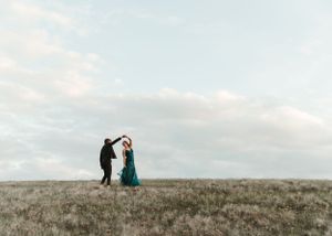 Couple dancing together on an open grassy plain under a cloudy sky. Senior grad photos. Graduation photos.