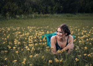 Smiling young woman in teal dress lying in a field of yellow wildflowers. Senior grad photos. Graduation photos.