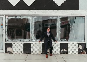 Young man posing confidently in front of a storefront with black and white geometric decor. Senior grad photos. Graduation photos.