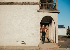 Young woman posing under arch of white brick building. Senior grad photos. Graduation photos.