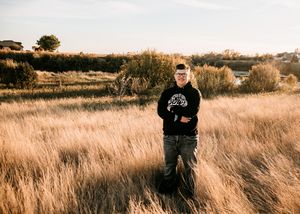 Teen boy in hoodie standing in golden autumn field. Senior grad photos. Graduation photos.