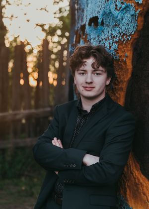Young man in a dark suit leaning against a rusty surface at golden hour. Senior grad photos. Graduation photos.