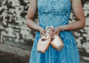 Close-up of woman in blue lace dress holding ballet pointe shoes with ribbon. Senior grad photos. Graduation photos.
