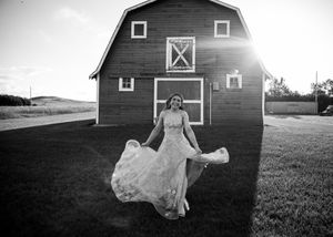 Black and white photo of a woman twirling in a gown outside a red barn at sunset. Senior grad photos. Graduation photos.