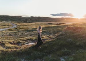 Woman in black dress walks through a vast green landscape bathed in warm golden sunset light. Senior grad photos. Graduation photos.