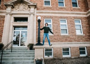 Young man jumping on lamppost outside brick building. Senior grad photos. Graduation photos.