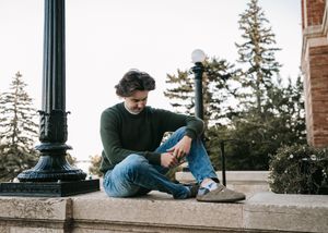 Casual man in green sweater sitting on stone ledge. Senior grad photos. Graduation photos.