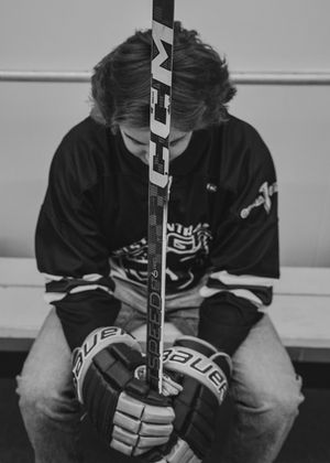 Black and white portrait of hockey player holding CCM stick with Bauer gloves in locker room. Senior grad photos. Graduation photos.