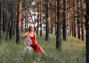Woman in red dress sitting on chair in pine forest. Senior grad photos. Graduation photos.