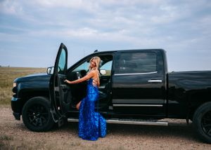 Woman in blue sequin gown stepping out of black truck outdoors. Senior grad photos. Graduation photos.