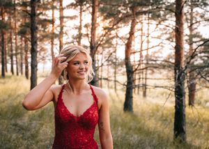 Young woman in red sequin gown posing in sunlit pine forest. Senior grad photos. Graduation photos.