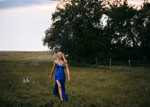 Woman in royal blue sequin gown walking through green meadow at dusk. Senior grad photos. Graduation photos.