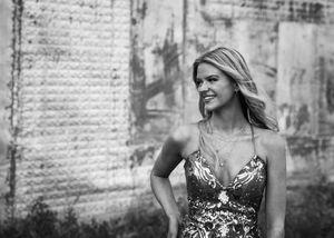Blonde woman smiling in patterned dress by rustic wall. Senior grad photos. Graduation photos.