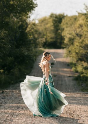 Woman twirling in elegant green floral tulle gown on a sunlit tree-lined dirt road. Senior grad photos. Graduation photos.