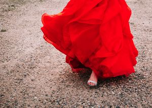 Close-up of a flowing red ballgown skirt with bare feet on gravel ground. Senior grad photos. Graduation photos.