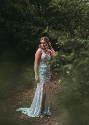 Woman in silver sequin formal gown posing on forest path surrounded by lush green trees. Senior grad photos. Graduation photos.