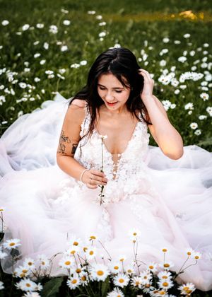 Bride in floral wedding gown sitting in daisy field. Senior grad photos. Graduation photos.