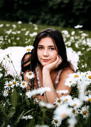 Young woman with dark hair lying in daisy field.