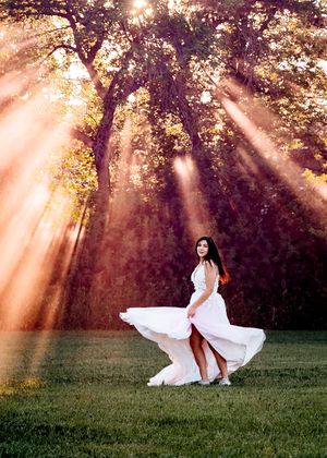 Woman in white dress twirling in sunlit forest. Senior grad photos. Graduation photos. Smoke bomb.
