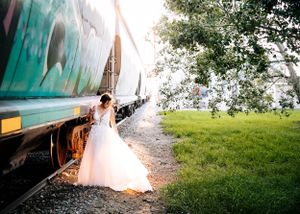 Bride in white wedding gown standing beside a colorful graffiti train outdoors. Senior grad photos. Graduation photos.