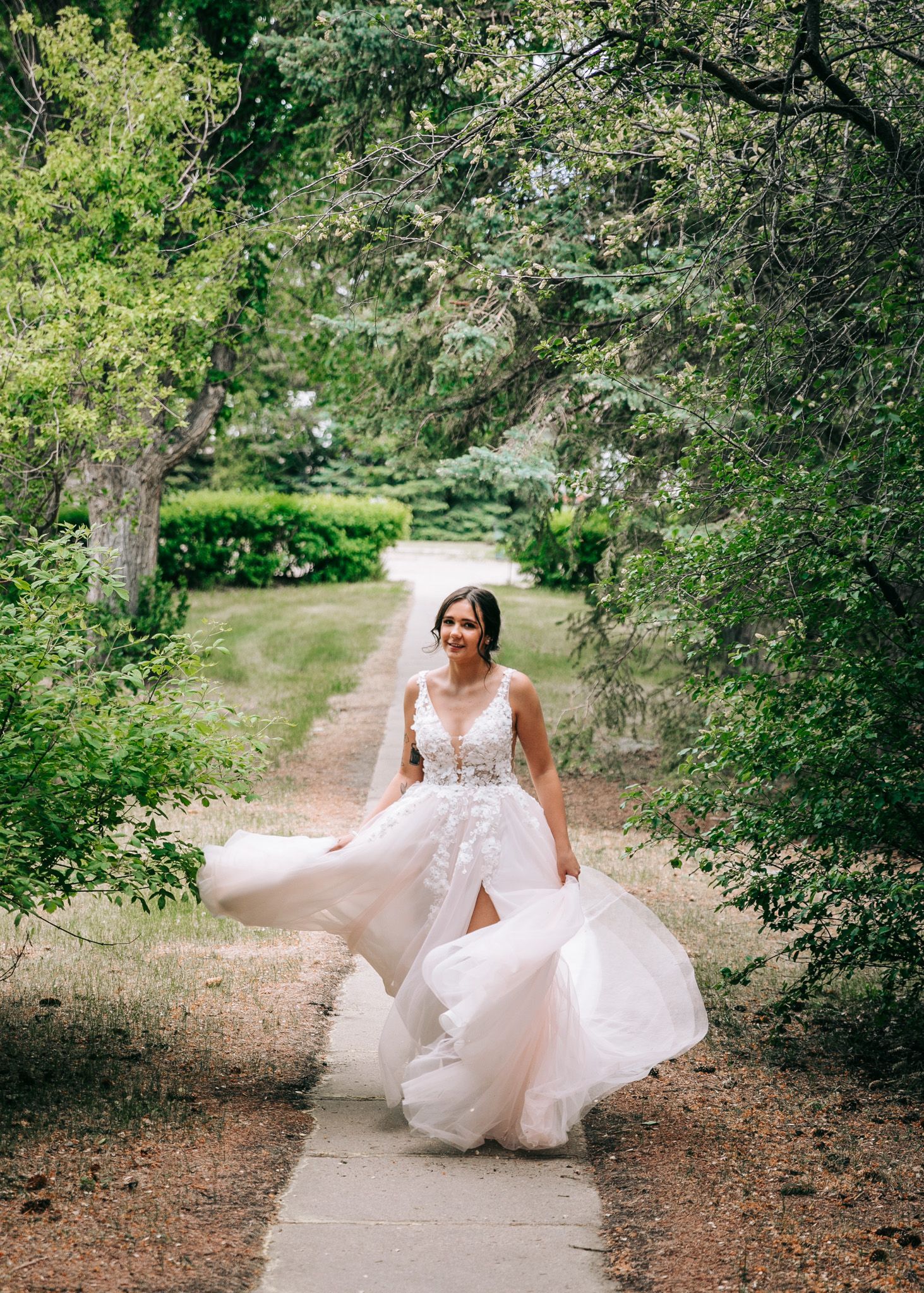 Bride in lace gown walking tree-lined garden path. Senior grad photos. Graduation photos.