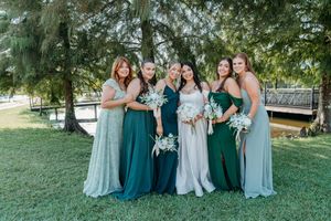 A bridal party wearing emerald green and light blue dresses poses together on a grassy hillside outdoors.