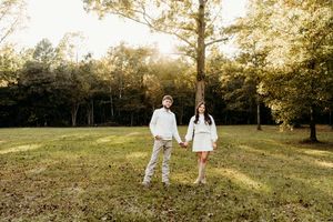 A couple in white outfits walks through a sunlit meadow during golden hour at a park.