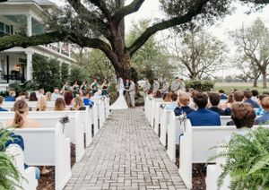 White outdoor wedding ceremony setup with wooden chairs and a majestic oak tree creating a natural canopy. 
wedding venue
