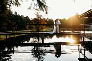 A serene lakeside wedding ceremony setup with white chairs and a gazebo reflecting in calm waters at sunset.