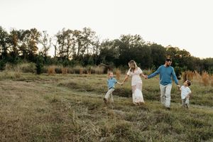 A family runs and plays together in a golden field at sunset during a lifestyle photography session.
