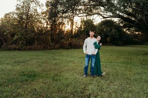 A couple stands with their dog in a grassy field during golden hour sunset.