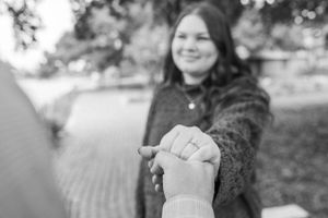 A close-up black and white photo showing hands with an engagement ring.