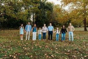 A group of people wearing coordinated blue and white outfits stand together on fallen autumn leaves in a park setting.