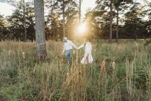 A couple walking through tall grass in a pine forest backlit by golden sunlight.