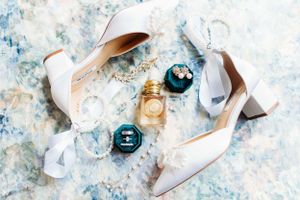 White wedding shoes and perfume bottles arranged on a marbled blue surface.