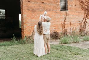 A couple stands outdoors near a rustic brick wall, their arms raised in a moment of joyful celebration.