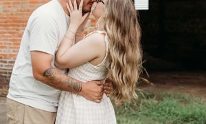 Young couple in white outfits sharing intimate moments outdoors in front of brick wall.