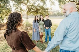 A chocolate Labrador retriever poses with a family during an outdoor autumn photoshoot in a sunlit park.