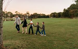 A line of people walking hand in hand across a grassy field at sunset.