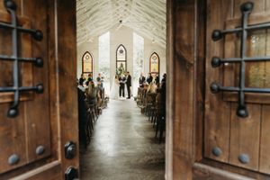 A view through wooden chapel doors showing a wedding ceremony in progress.