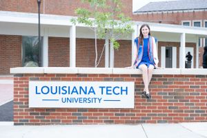Student sits on brick wall with Louisiana Tech University sign on campus.