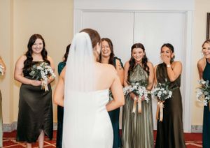 Wedding party in mix of green and black dresses holding bouquets indoors.