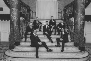 Groomsmen in black suits posed on grand marble staircase.