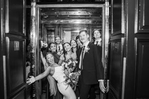 A joyful wedding party celebrating in a vintage elevator with dark wood paneling.