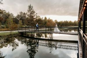 A couple in wedding attire poses on a wooden dock over a reflective pond surrounded by autumn trees.