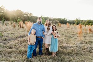 A family stands together in a golden field with pampas grass at sunset.