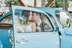 Bride and groom sharing a kiss inside a vintage blue car on their wedding day.
