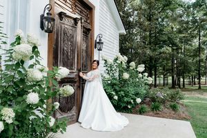 Elegant white chapel entrance adorned with blooming hydrangea bushes and ornate wooden doors in a serene woodland setting.